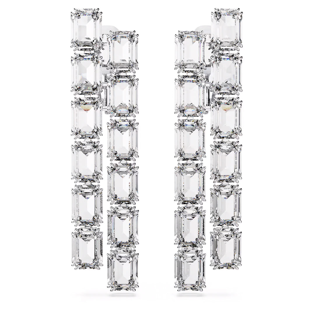 A close-up of the Swarovski Millenia Clip Earrings reveals their rectangular, multi-tiered geometric design. Enhanced by rhodium plating, these earrings showcase stunning octagon-cut crystals paired with multiple clear, emerald-cut stones arranged in vertical rows on a white background.
