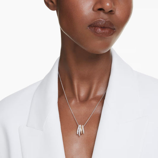 A person wearing a white blazer highlights the elegant design of the Swarovski Hyperbola Mixed Cuts Necklace Pendant, which features three vertical pendants in a mixed metal finish adorned with Swarovski Zirconia, set against a plain white background.