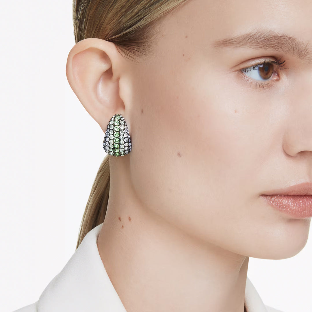 Close-up of a person wearing Swarovski Sumlima Drop Earrings adorned with marine crystals. The individual has light skin and blond hair pulled back, dressed in a white collared outfit, against a white background.