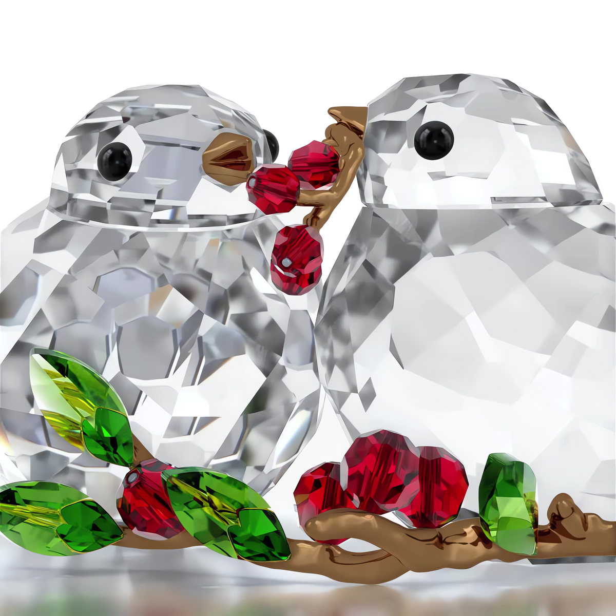 The Swarovski Idyllia Bird Couple and Berries by Swarovski features two sparkling crystallized birds facing each other, sharing red crystal berries. Surrounded by green crystal leaves and golden branches, this charming decorative piece is inspired by an Idyllia garden and set against a simple white background.