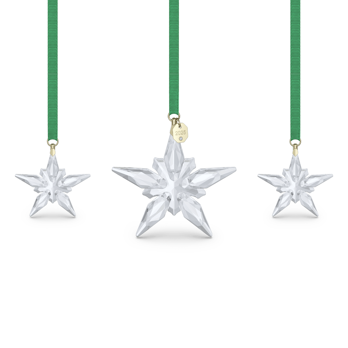 Three crystal star ornaments hang from green ribbons; the center ornament, part of the Swarovski Annual Edition Ornament Set 2025, features a gold tag engraved with “2025.” All ornaments are six-pointed and displayed against a plain white background—available from your Swarovski authorized retailer in Canada.