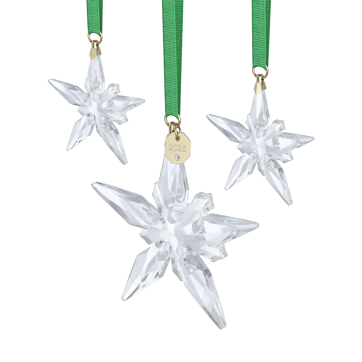 Three crystal star ornaments from the Swarovski Annual Edition Ornament Set 2025 hang from green ribbons. The front ornament features a small gold tag engraved with “2025.” This elegant set by Swarovski, available through authorized retailers, is displayed against a plain white background.