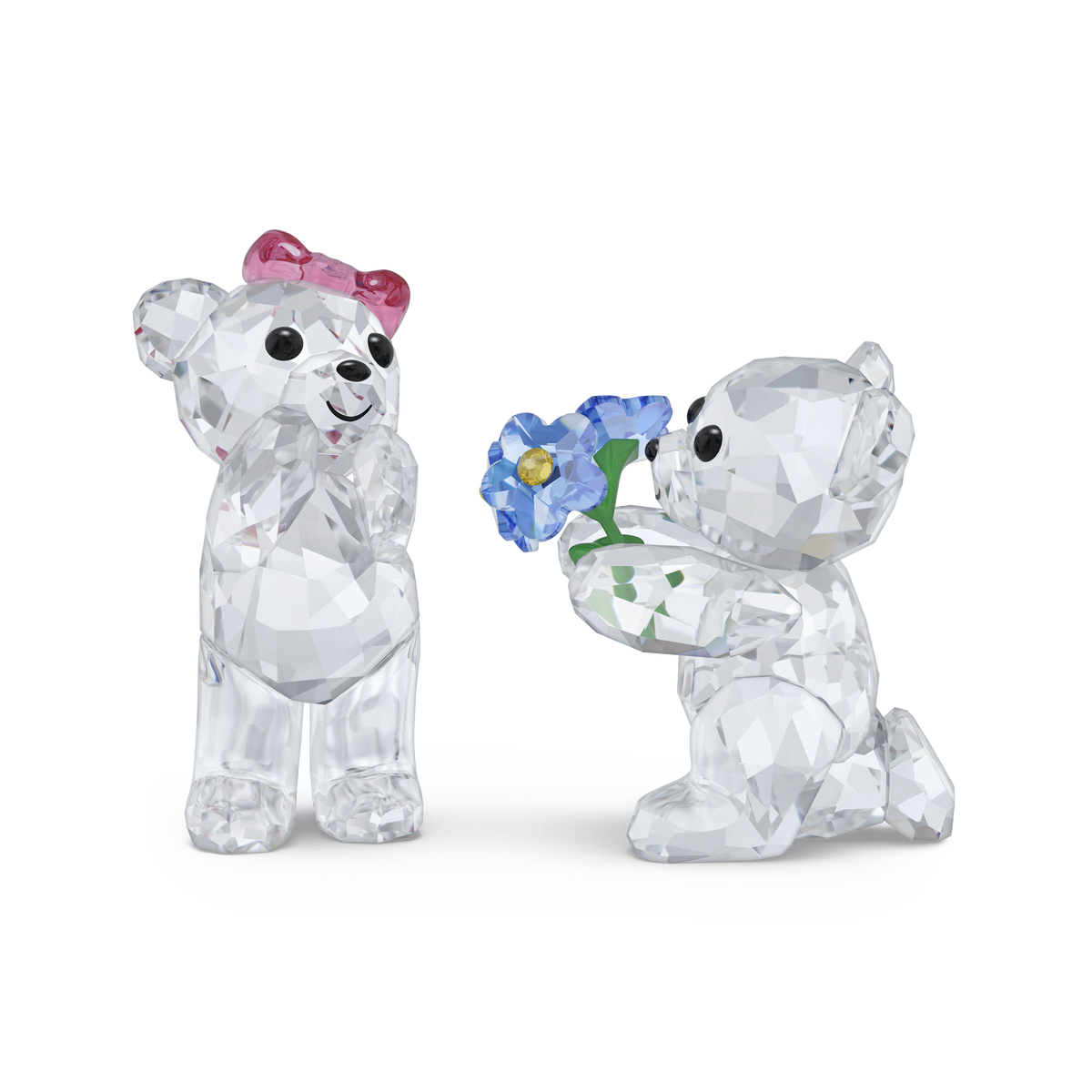 Swarovski Kris Bear I Adore You: Two charming crystal figurines by Swarovski, each with clear bodies and sparkling black eyes—one standing with a pink bow, the other kneeling and presenting blue flowers. Perfectly displayed against a plain white background, this romantic set makes an ideal gift for any occasion.