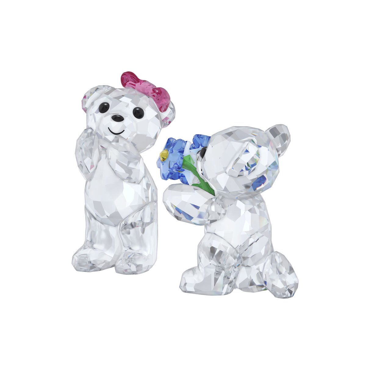 Two faceted crystal figurines from the Swarovski Kris Bear I Adore You collection—one standing with a pink bow, the other kneeling and holding blue flowers. Both bear a shiny finish, making them a charming romantic gift from Swarovski, presented against a plain white background.