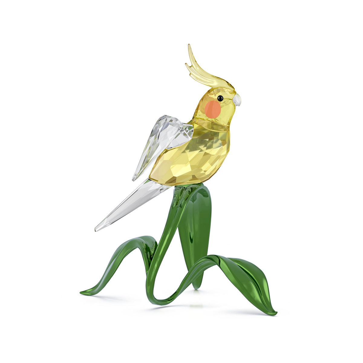 The Swarovski Idyllia Cockatiel by Swarovski features a charming glass cockatiel figurine with clear wings and orange cheeks, perched on glossy green glass leaves, creating an elegant crystal decoration set against a plain white background.