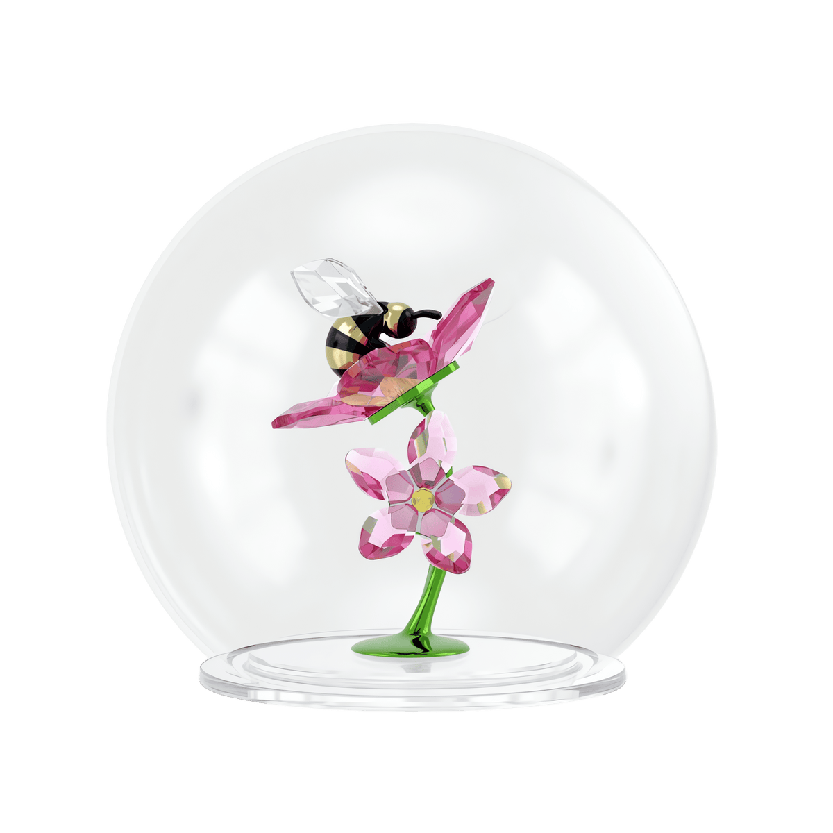 The Swarovski Idyllia Glass Ball Bee and Flowers by Swarovski features a delicate crystal bee figurine perched on a pink flower, with another pink flower below, all displayed on a green stem within a glass dome for an elegant floral decoration against a white background.