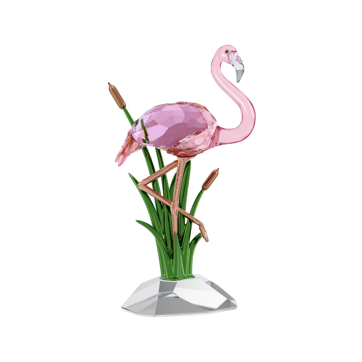 The Swarovski Idyllia Flamingo by Swarovski features a pink crystal flamingo poised on one leg among green reeds and brown cattails, all arranged on a clear faceted base with subtle rose gold-tone accents, creating a charming decorative object against a white background.