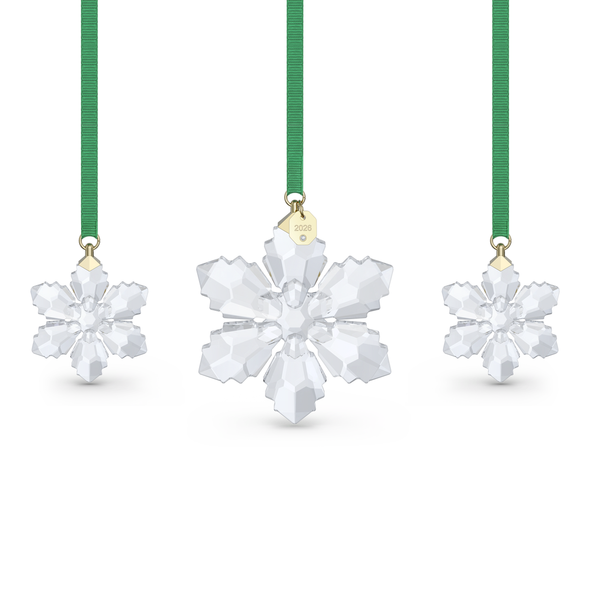 Three crystal snowflake ornaments with green ribbons from Swarovski are displayed against a white background. The center ornament features a gold tag marked “2026,” making this the stunning Swarovski Annual Edition Ornament Set 2026 and an elegant holiday decoration.