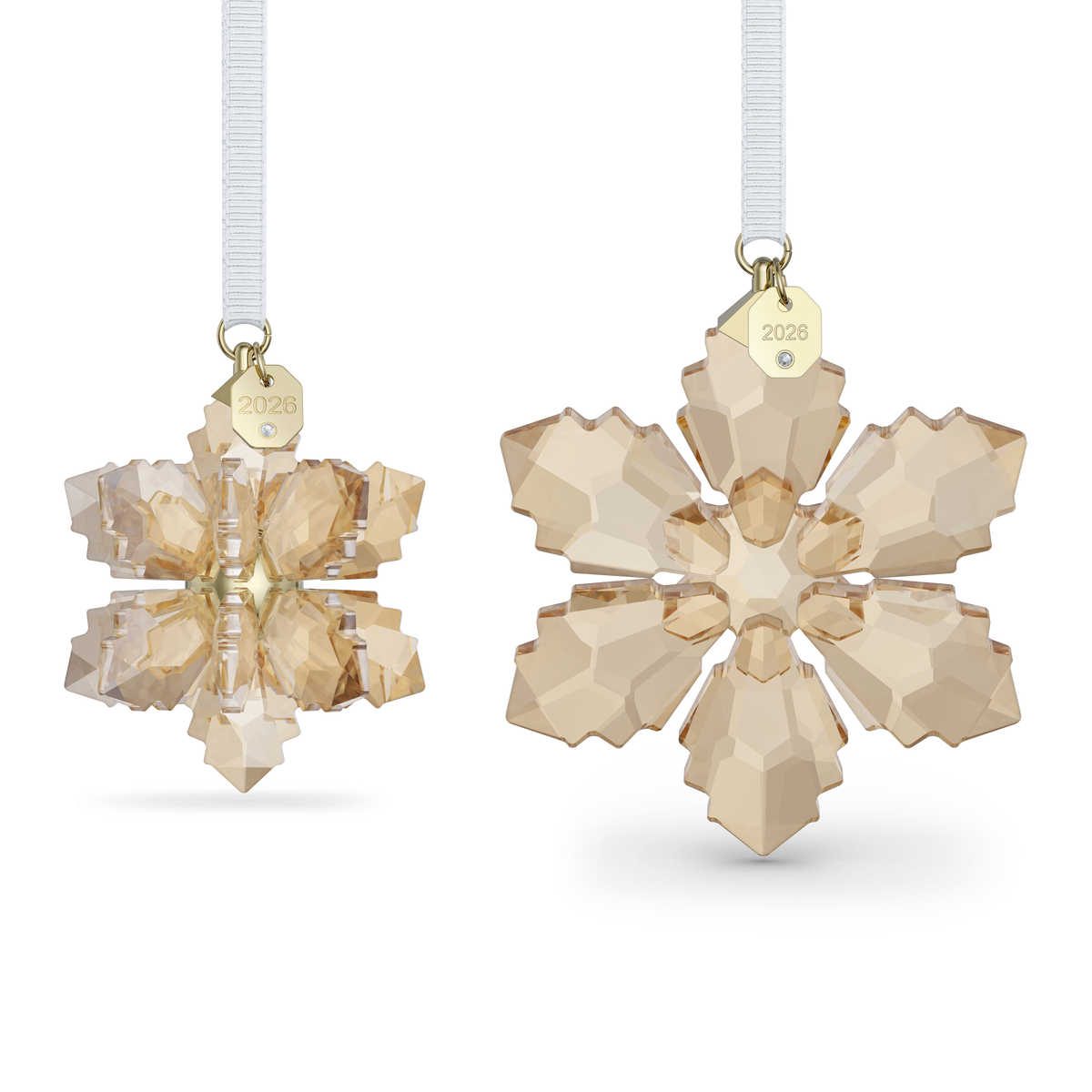 Two gold-toned crystal snowflake ornaments—part of the Swarovski Annual Edition Festive 3D Ornament Set 2026—feature white ribbons and small gold tags engraved with “2026,” shown from side and front views against a white background.