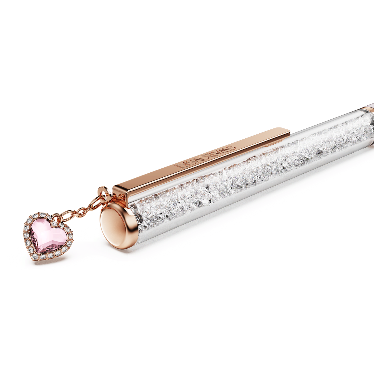 The Swarovski Crystalline ballpoint pen in pink lacquer features a rose gold-tone plated clip and cap, filled with sparkling clear crystals. A pink heart charm bordered with shimmering rhinestones hangs gracefully from the top, infusing the design with signature Swarovski glamour. The background is plain white.