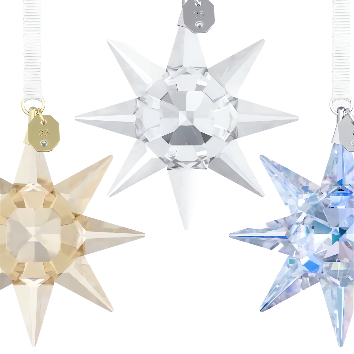 Celebrate the season with the Swarovski Annual Edition 35th Anniversary Ornament Set 2026. This exquisite set features three faceted crystal star ornaments in gold, clear, and blue tones, each suspended from a white ribbon against a pristine white background to evoke the shimmering elegance of Aurora Boreale. Perfect as holiday ornaments, each piece captures the brilliance and timeless beauty for which Swarovski is renowned.