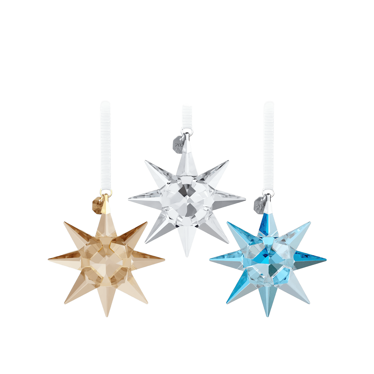 Three faceted, star-shaped crystal ornaments from the Swarovski Annual Edition 35th Anniversary Ornament Set 2026—crafted in gold, clear, and blue hues—hang from white ribbons against a simple white background. Each ornament channels the elegance of Aurora Boreale and is adorned with a small metallic charm near the top, capturing the signature brilliance of Swarovski’s celebrated holiday stars.