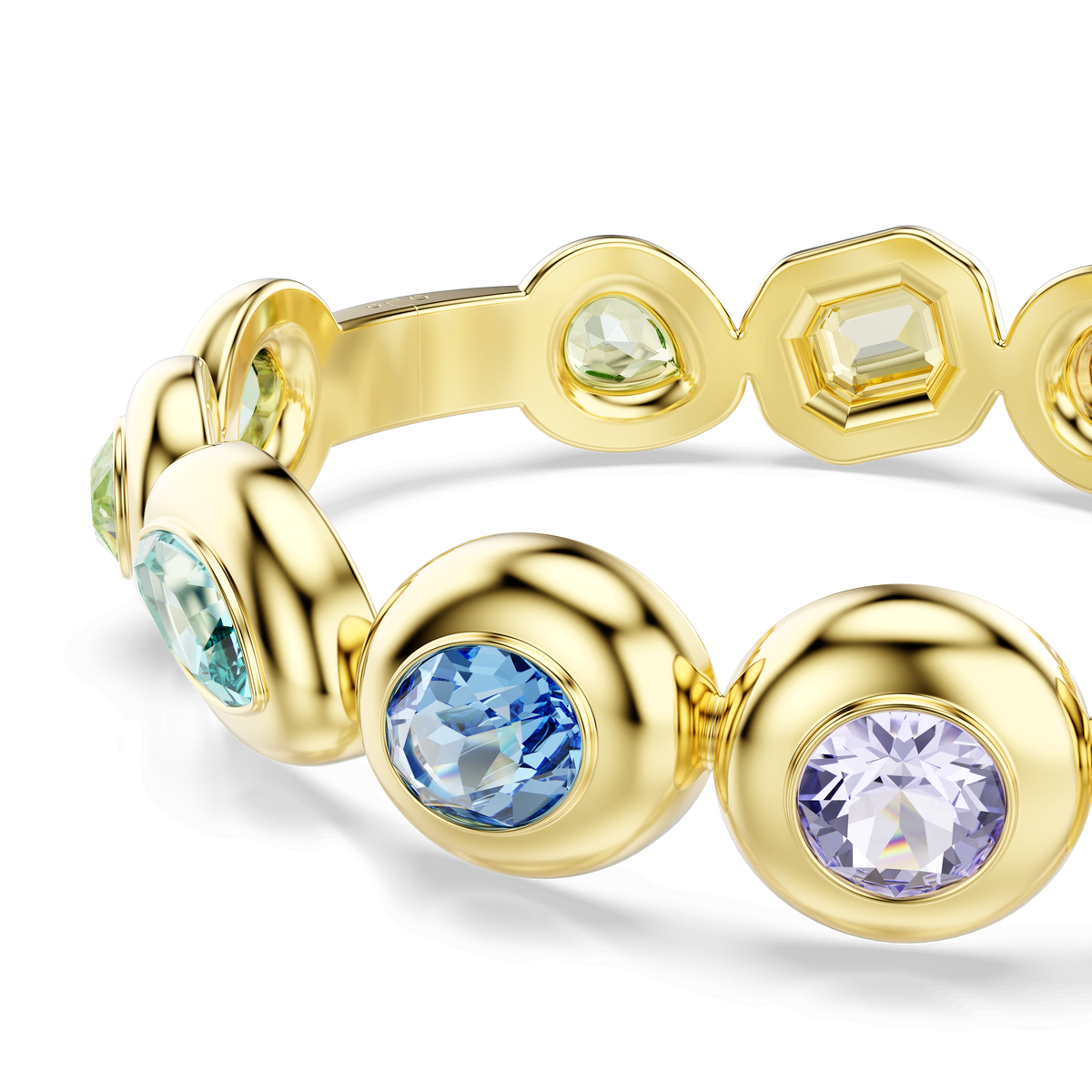 The Swarovski Gema bangle, crafted with an 18K gold finish, showcases mixed-cut multicolored gemstones—including round, bezel-set blue, green, and lavender stones—accented by asymmetrical crystals and elegantly displayed against a white background.