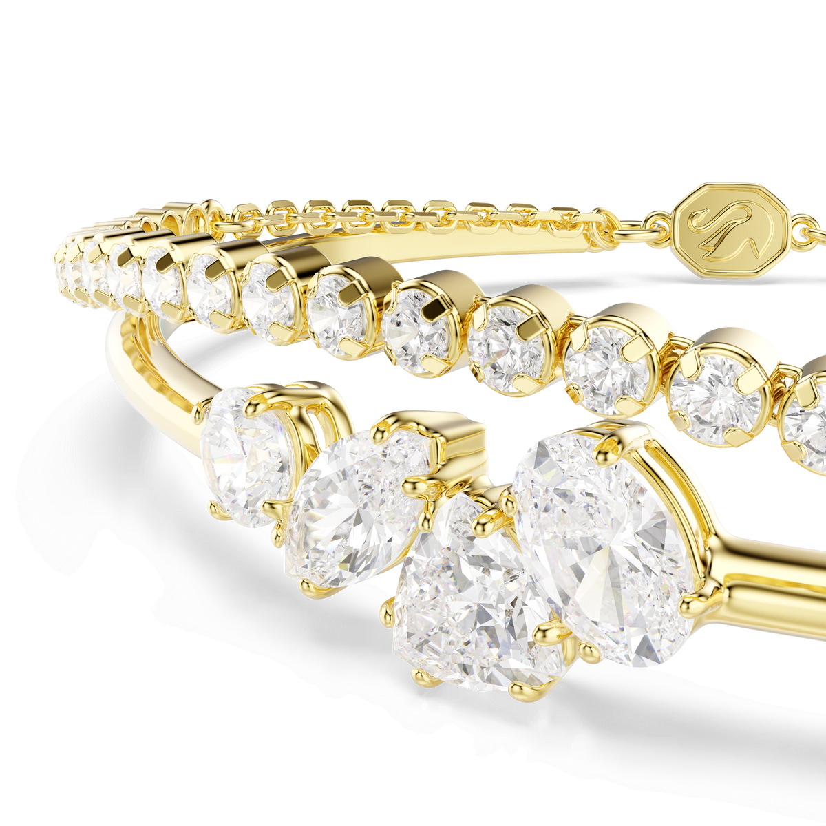Two Swarovski Mesmera bracelets with an 18K gold finish, adorned with large round and oval white Swarovski Zirconia in mixed cuts, are displayed on a white background. This striking Swarovski jewelry includes a bracelet featuring a small gold tag engraved with a letter, perfect for creating a stylish layered look.