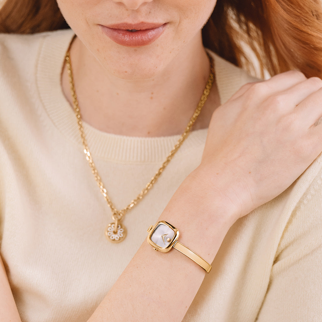 A woman wearing a gold PVD Movado Museum Bangle Quartz 21.5mm Watch featuring a minimalist mother-of-pearl dial with a single dot at the twelve o’clock position.