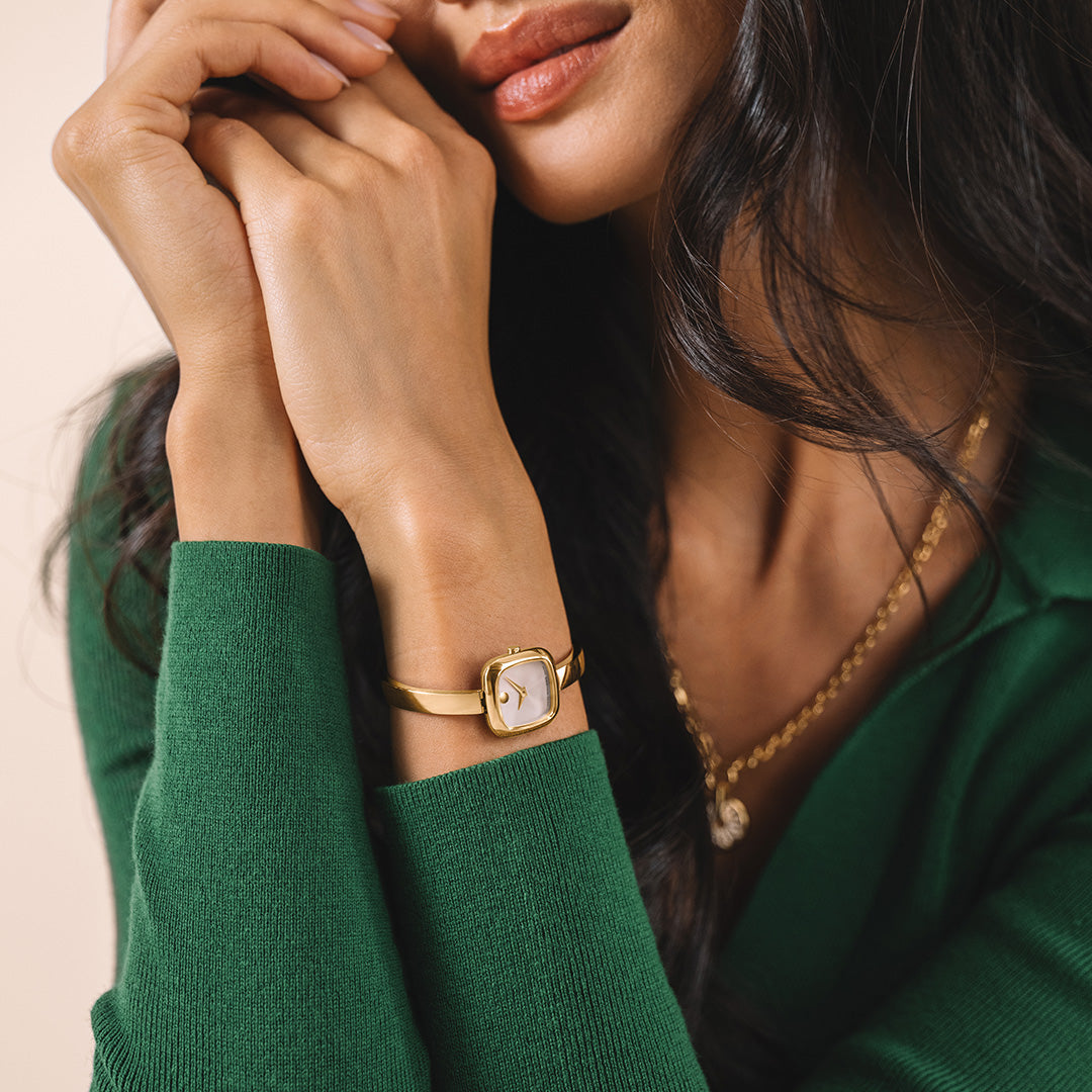 A square-faced gold Movado Museum Bangle Quartz 21.5mm Watch with a single dot at the twelve o’clock position, worn on a thin gold PVD bangle bracelet.