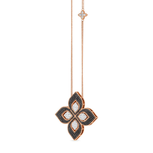 The Roberto Coin Venetian Princess necklace features an exquisite large flower pendant crafted from 18K rose gold. This elegant piece showcases black and white diamonds, enhancing the intricate floral design of the pendant. Additional diamond-accented matching floral motifs are elegantly spaced along the chain, adding a touch of sophistication to this captivating necklace.