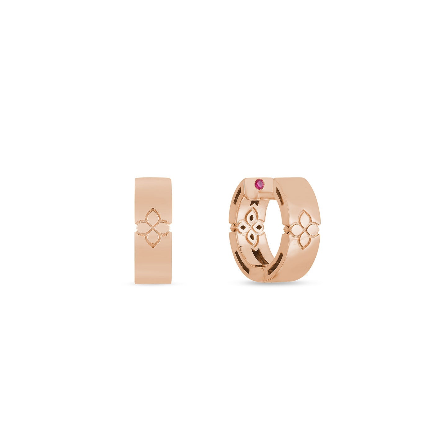 Displayed are two matching rose gold huggie earrings that feature a decorative design, with one earring set with a small red gemstone. These earrings, crafted in the elegant Verona style, boast a smooth and shiny finish synonymous with Roberto Coin's exquisite jewelry collections.