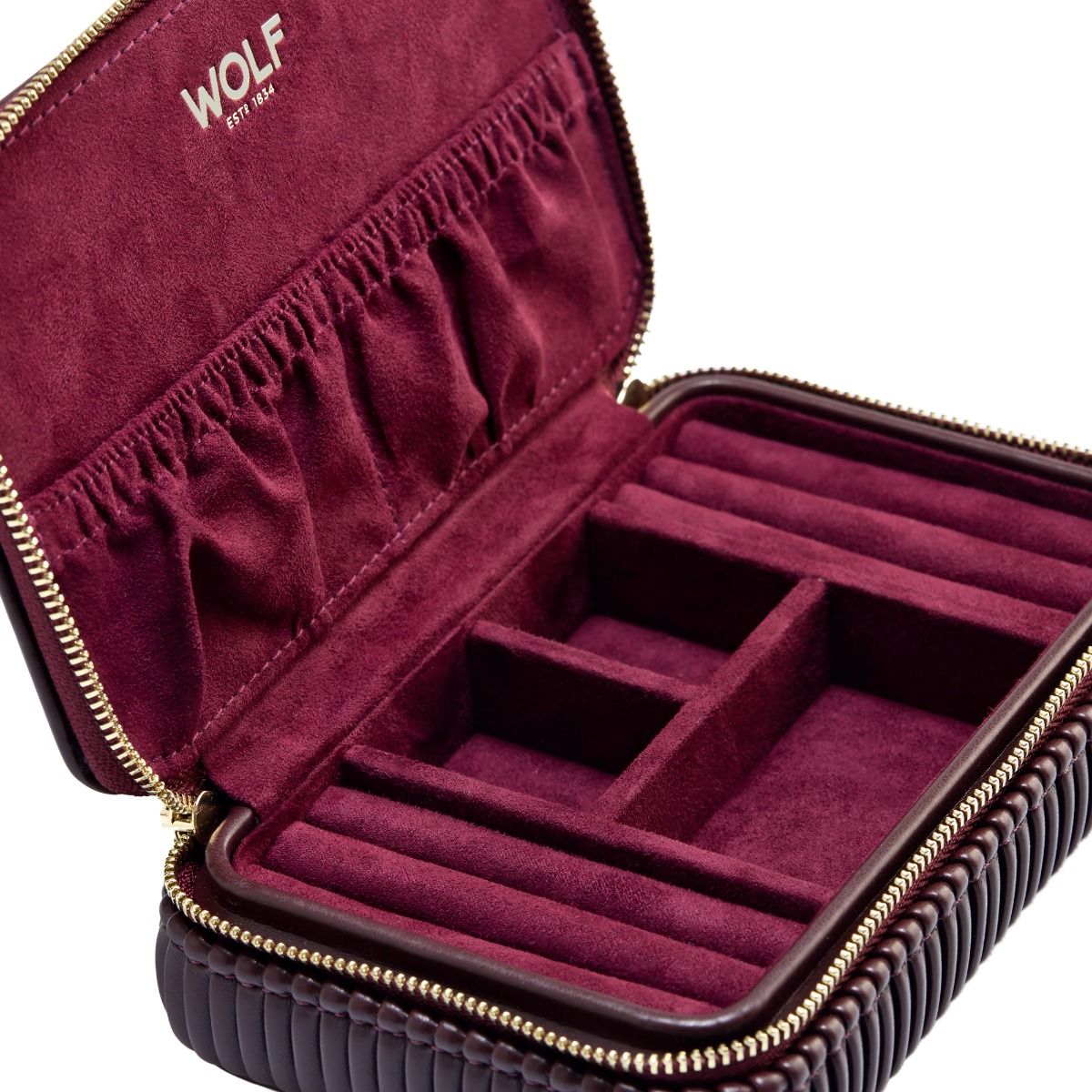 The WOLF 1834 Bella Zip Jewellery Case by WOLF is a burgundy vegan case with a zip closure, featuring plush-lined compartments and ring rolls for organized jewelry storage.