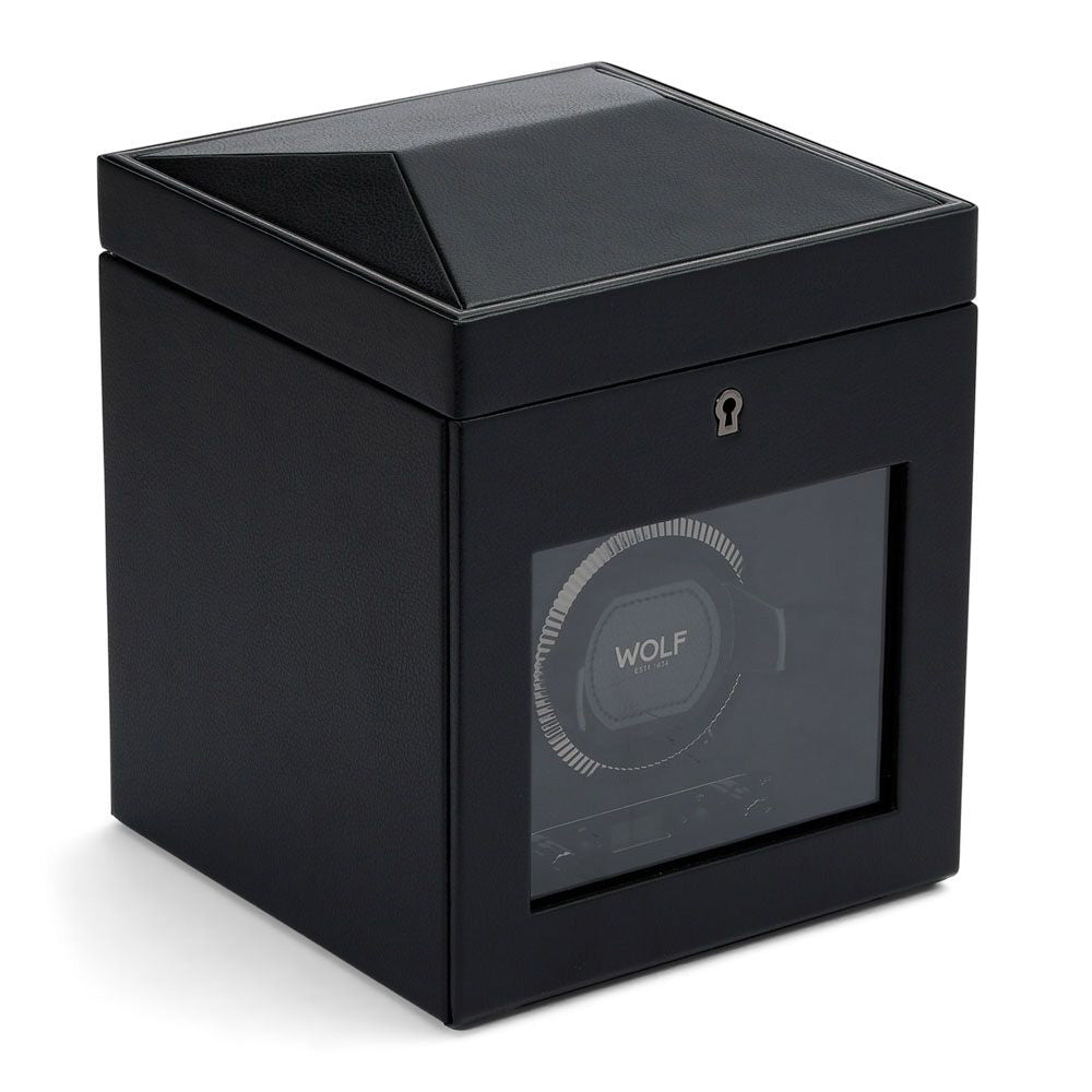 The WOLF 1834 British Racing Double Watch Winder With Storage is designed with a sleek black, cube-shaped exterior featuring a transparent front panel to showcase its internal mechanism. It provides various rotation options and includes a keyhole for secure locking. The winder also integrates WOLF's patented lock-in dynamic cuff and prominently displays the brand name inside.