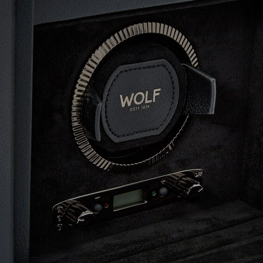 Close-up of a WOLF 1834 British Racing Double Watch Winder with the brand name "WOLF" and "EST 1834" embossed in the center. Boasting multiple rotation options, its elegant circular design includes a digital control panel below. The textured black interior and patented lock-in dynamic cuff enhance its luxurious appeal.