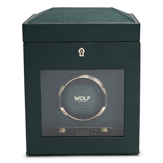 The WOLF 1834 British Racing Green Single Winder boasts a sleek design with a clear display window that reveals the intricate interior mechanism. Its exterior is textured to resemble vegan leather, and it features a small keyhole at the top center, enhancing its elegant British Racing theme.