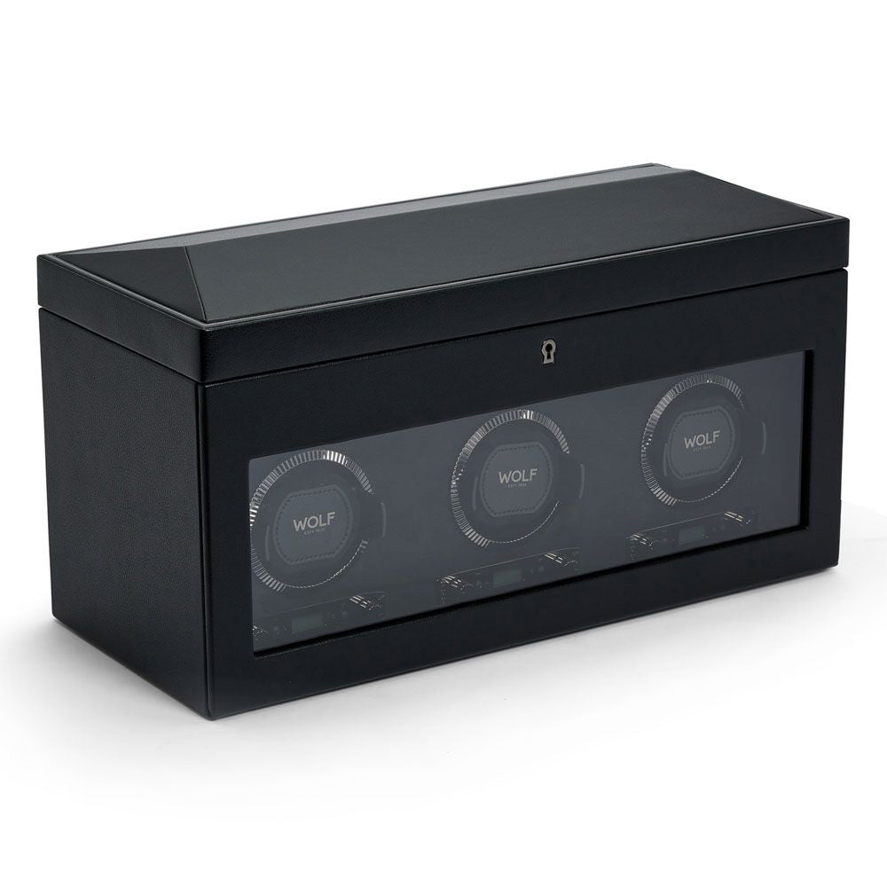 The WOLF 1834 British Racing Triple Watch Winder With Storage is an elegant black automatic watch winder featuring a patented design and a glass window that displays three slots, each adorned with the "Wolf" name. The watch winder showcases a minimalist case with subtle texture and includes a small lock on the front, providing multiple rotation settings for optimal watch care.