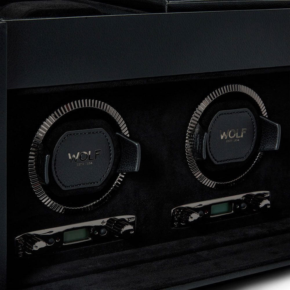 Close-up of the WOLF 1834 British Racing Triple Watch Winder With Storage, displaying patented innovation with two rotating slots containing textured leather holders embossed with "WOLF EST. 1834." Below each slot is a control panel equipped with buttons and a digital display for selecting various rotation options. The surface is sleek and polished.
