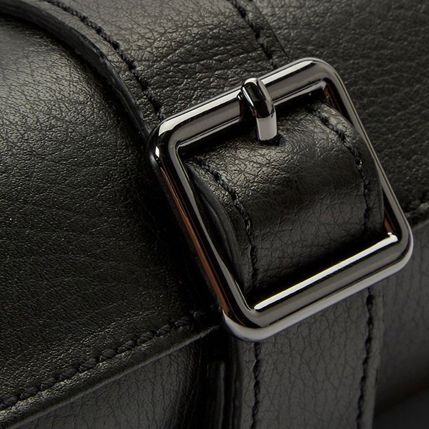 Close-up of the WOLF 1834 British Racing Triple Watch Rolls, showcasing a shiny, square metallic buckle. The texture of the black leather is visible, emphasizing the craftsmanship and design details that echo a luxurious jewelry capsule.