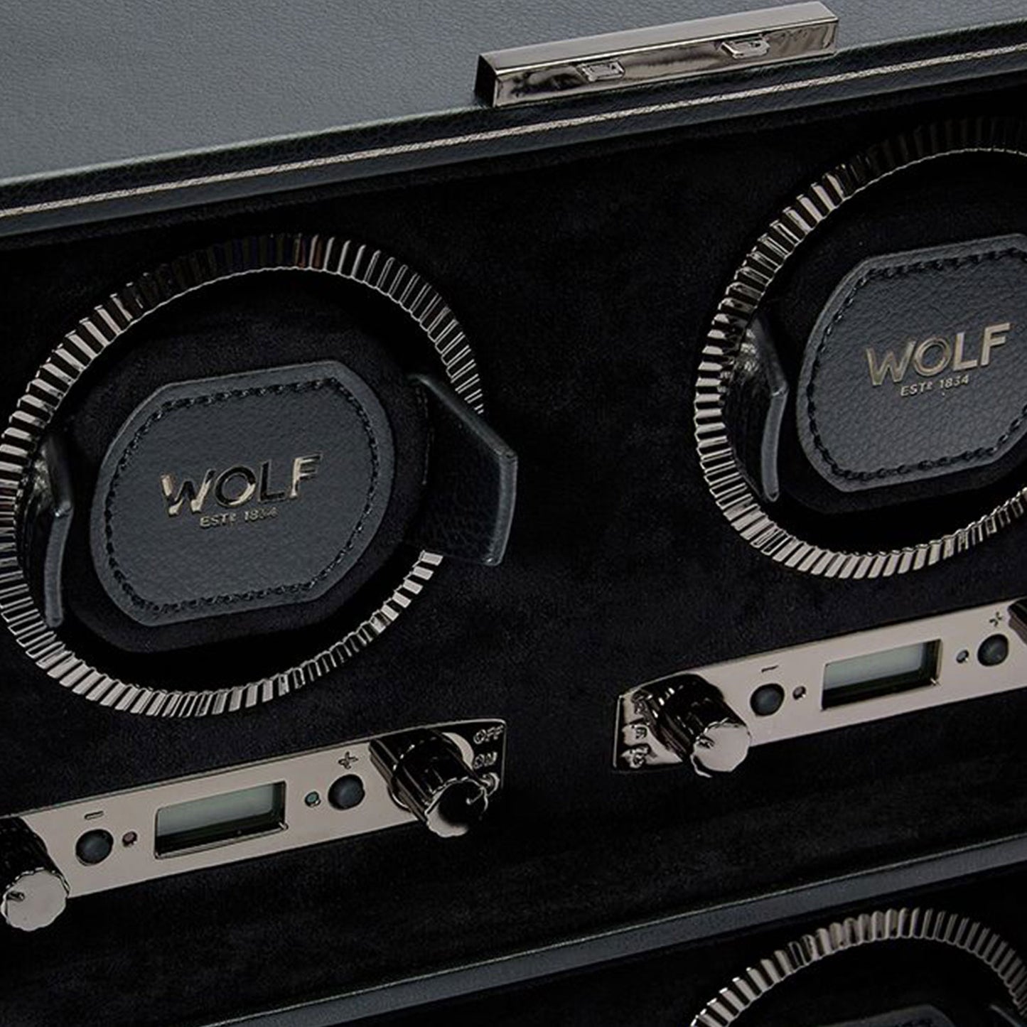 A close-up of the WOLF 1834 British Racing 4PC Watch Winder showcases "Est. 1834" embossed on its black leather interior. This device exudes timeless elegance with silver dials and digital displays, embodying the sophistication of British Racing.