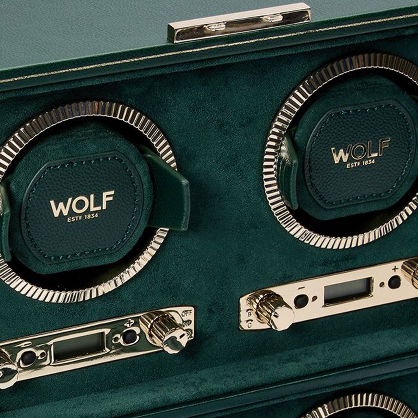 Close-up of the WOLF 1834 British Racing 4PC Watch Winder in luxurious green, showcasing "WOLF" and "EST 1834" on its rotating bezels. This classic piece features metallic controls and detailed dials for adjusting settings, embodying the elegance of British Racing heritage.