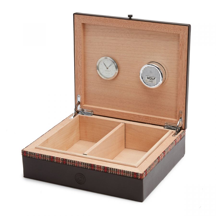 The WOLF 1834 WM Brown Humidor is a sophisticated watch box with two compartments, showcasing a wooden interior and dark exterior. Crafted for the modern man, it integrates a built-in clock and features a circular panel adorned with the "WOLF" branding. A plaid accent graces the rim, adding an element of timeless fashion.