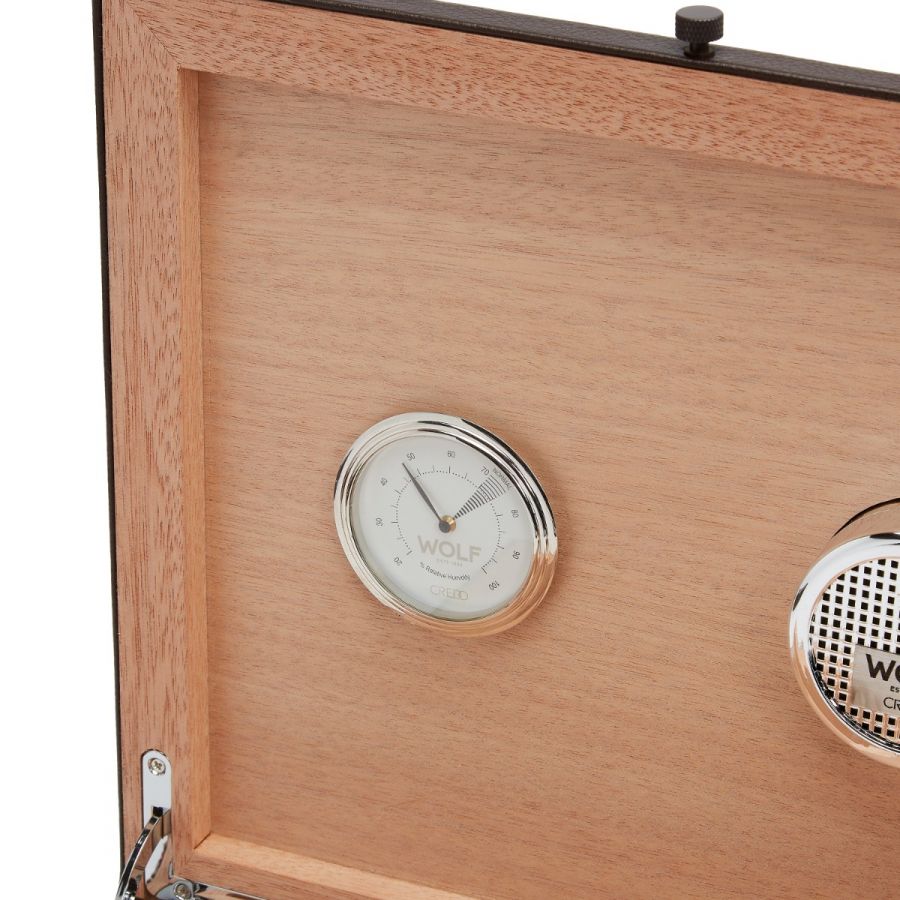 A close-up of the interior of the WOLF 1834 WM Brown Humidor showcases a hygrometer and speaker. The silver dials feature a minimal design, and the wood boasts a light, natural finish, highlighting the elegance of this collaboration with WOLF.