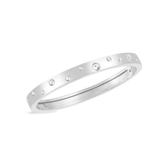 The Roberto Coin Pois Moi Luna Bangle showcases a sophisticated design crafted from 18K White Gold, adorned with small circular studs and round diamonds artfully embedded across its surface, all set against a plain white backdrop.