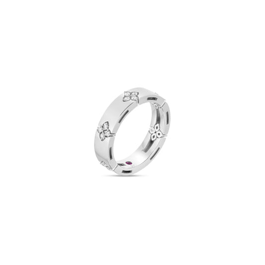 The Roberto Coin Love In Verona 18K White Gold Diamond Ring beautifully displays small floral motifs adorned with tiny diamonds around its band. Inside, it features a small, round ruby inlay. This exquisite piece by Roberto Coin is set against a white background, highlighting its intricate details and timeless elegance.