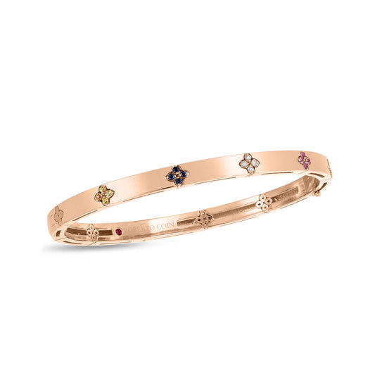 The Roberto Coin Love In Verona 18K White Gold Diamond and Sapphire Bracelet is an exquisite piece featuring a polished finish and delicate detailing along its edges. It is adorned with small, colorful round sapphires set in a charming floral design pattern around its surface.