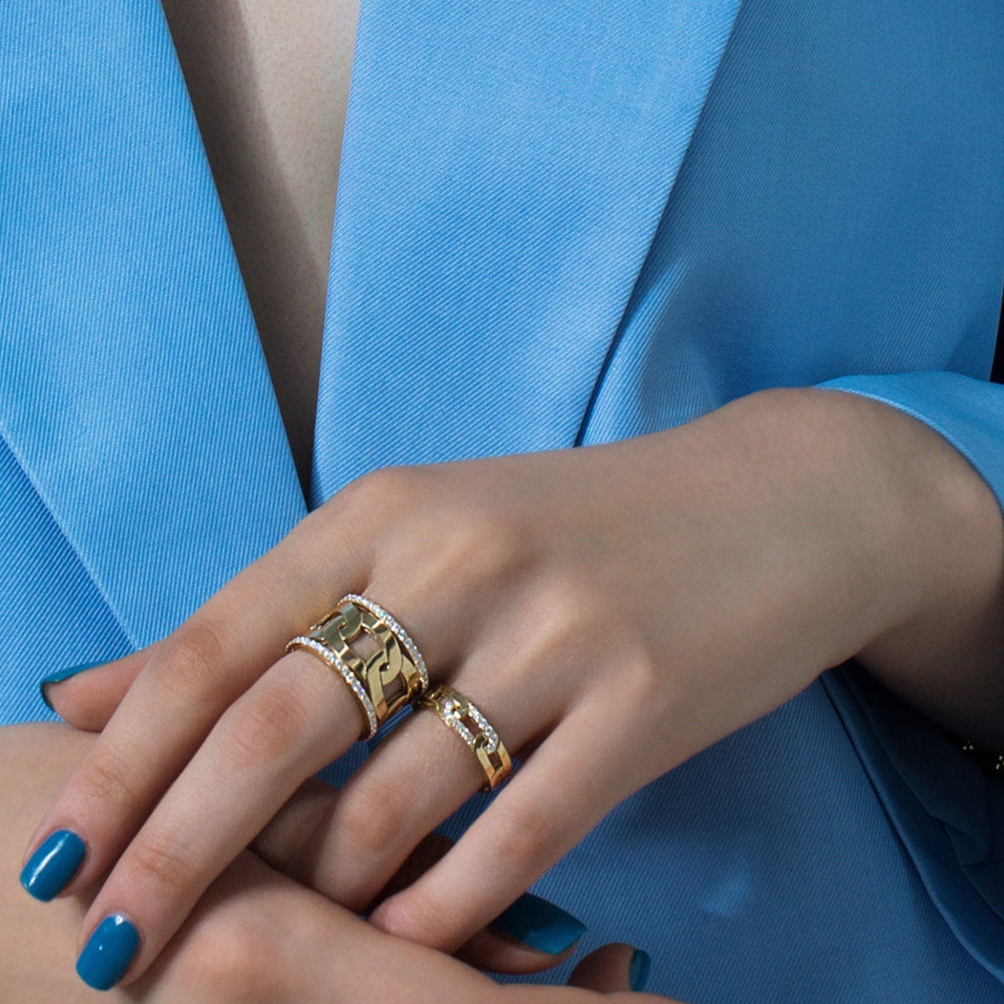 A person wearing a blue blazer is showcasing two gold rings on their fingers, including the stunning Roberto Coin Navarra 18K Yellow Gold Slim Ring. These elegant rings perfectly complement their nails, painted in matching blue.