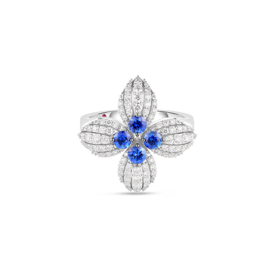 The Roberto Coin Love in Verona 18K White Gold Diamond and Blue Sapphire Flower Ring features a floral design with five round blue sapphires at the center, surrounded by intricate petal-like arrangements of clear crystals. The band is elegantly visible beneath the design, adding a touch of sophistication.