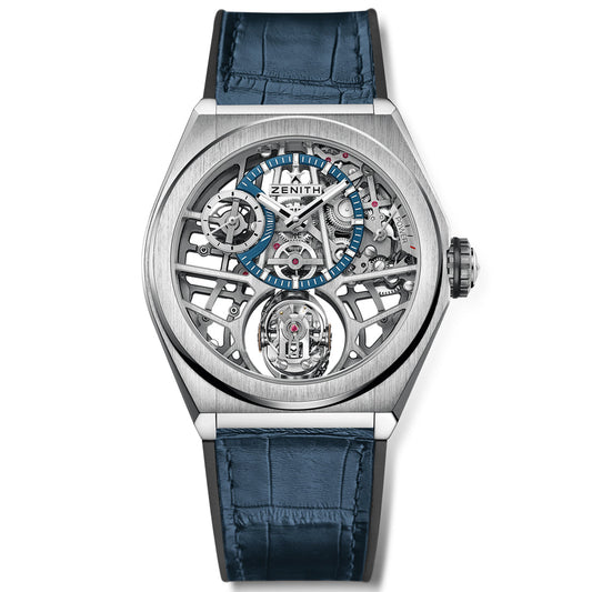 The ZENITH Defy Zero G El Primero 8812 S 44mm Watch flaunts a silver skeleton movement face with visible intricate gears, a blue hour marker ring, and a blue leather strap. The Zenith brand name crowns the top center, highlighting its gyroscopic innovation.