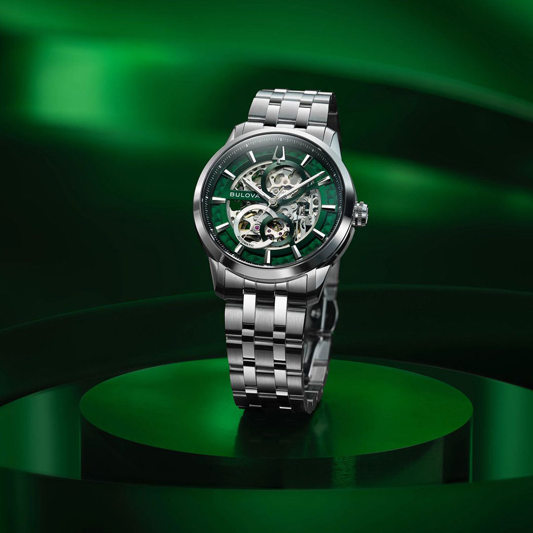 The Bulova Sutton Classic Automatic 40mm men's watch, featuring a stainless steel bracelet and green skeleton dial, is showcased on a green circular platform with a matching abstract green background.