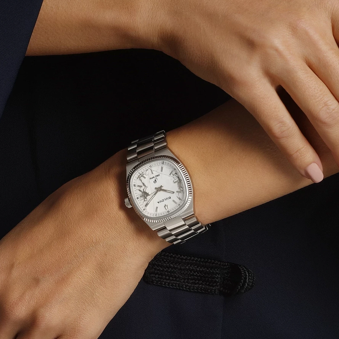 A Bulova Super Seville Precisionist Quartz 35mm Watch on a wrist, featuring a retro-inspired silver-tone design, fluted bezel, white dial, and stainless steel bracelet.