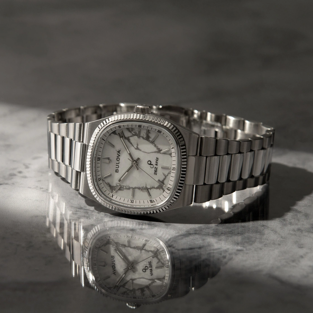 Bulova Super Seville Precisionist Quartz 35mm Watch with a silver-tone rectangular case, white marble-patterned dial, and stainless steel bracelet, reflecting on a marble surface.