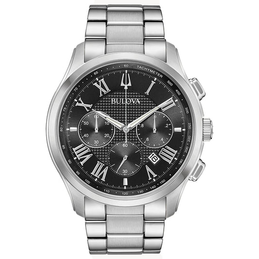 The Bulova Wilton Quartz 46.5mm Watch has a silver stainless steel bracelet and case, featuring a black textured dial with Roman numeral markers, three sub-dials, a date window at 4 o'clock, three hands, and a tachymeter scale on the bezel.