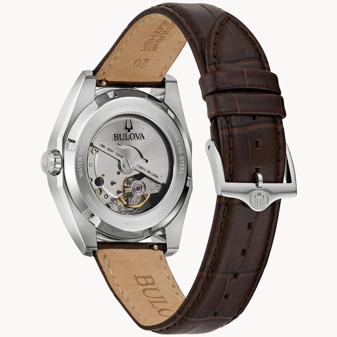 The image displays the back of the Bulova Surveyor Automatic 39mm Watch, highlighting its stainless steel case and a brown leather strap with a silver buckle. The transparent caseback elegantly reveals the automatic 21-jewel movement within, showcasing its intricate inner workings.