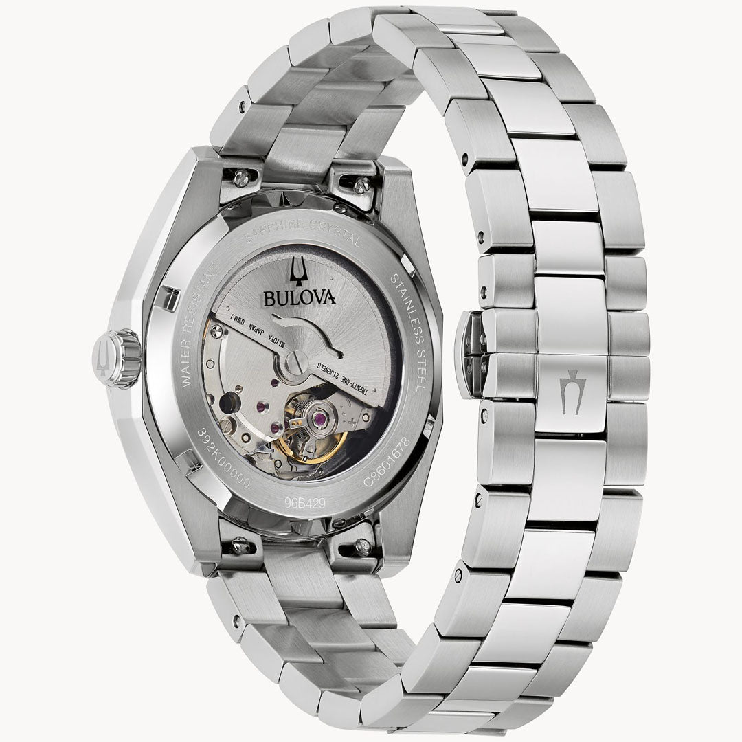 The Bulova Surveyor Automatic 39mm Watch, a silver men's timepiece, features an open back casing that reveals its intricate 21-jewel automatic movement. Its polished stainless steel bracelet includes a clasp with the Bulova logo and has "stainless steel" engraved on the back.