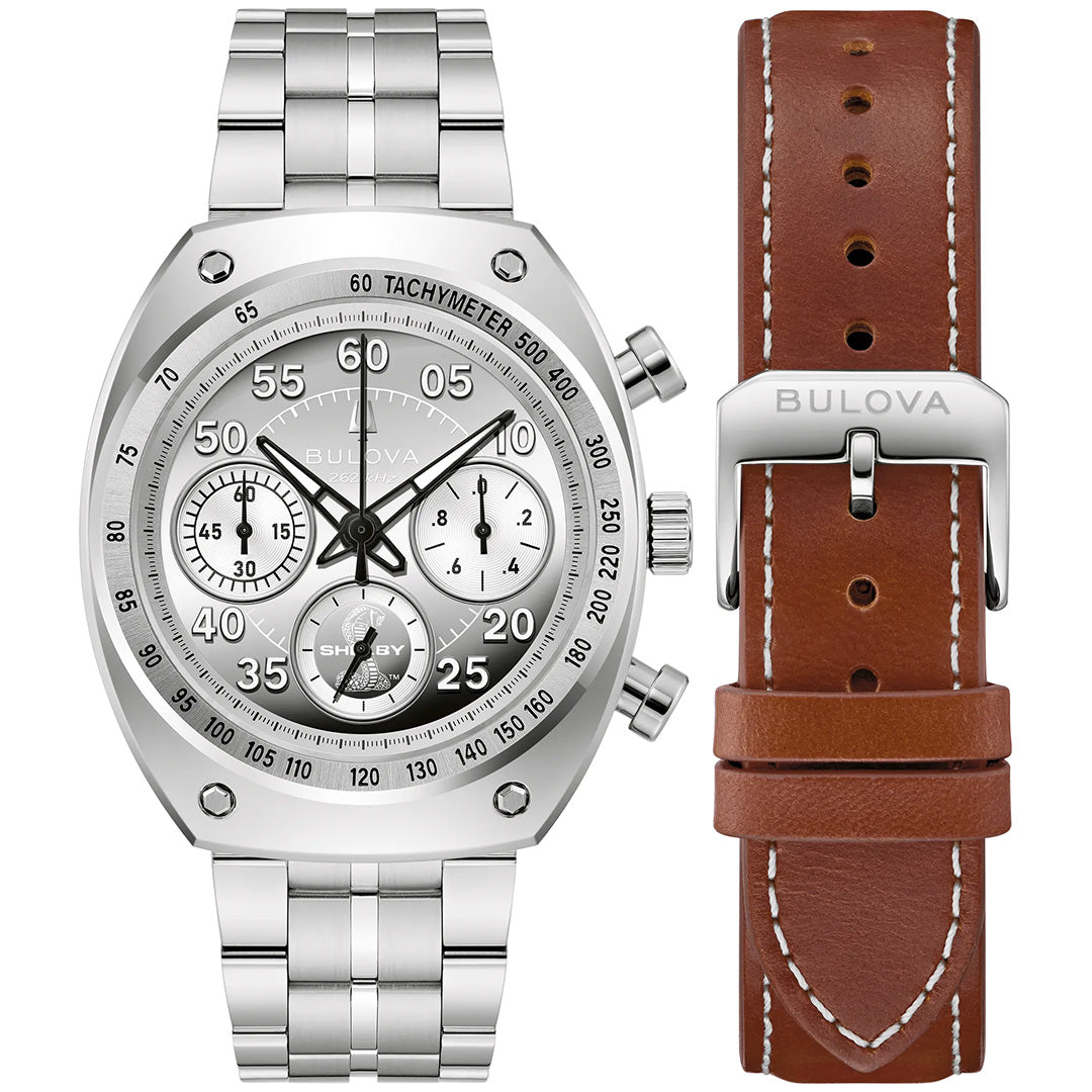 A Bulova Shelby Racer Chronograph Quartz 40.5mm Watch Limited Edition is displayed with a silver metal band, alongside a brown leather strap with white stitching and a metal buckle engraved with “Bulova.”.