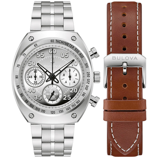 A Bulova Shelby Racer Chronograph Quartz 40.5mm Watch Limited Edition is displayed with a silver metal band, alongside a brown leather strap with white stitching and a metal buckle engraved with “Bulova.”.