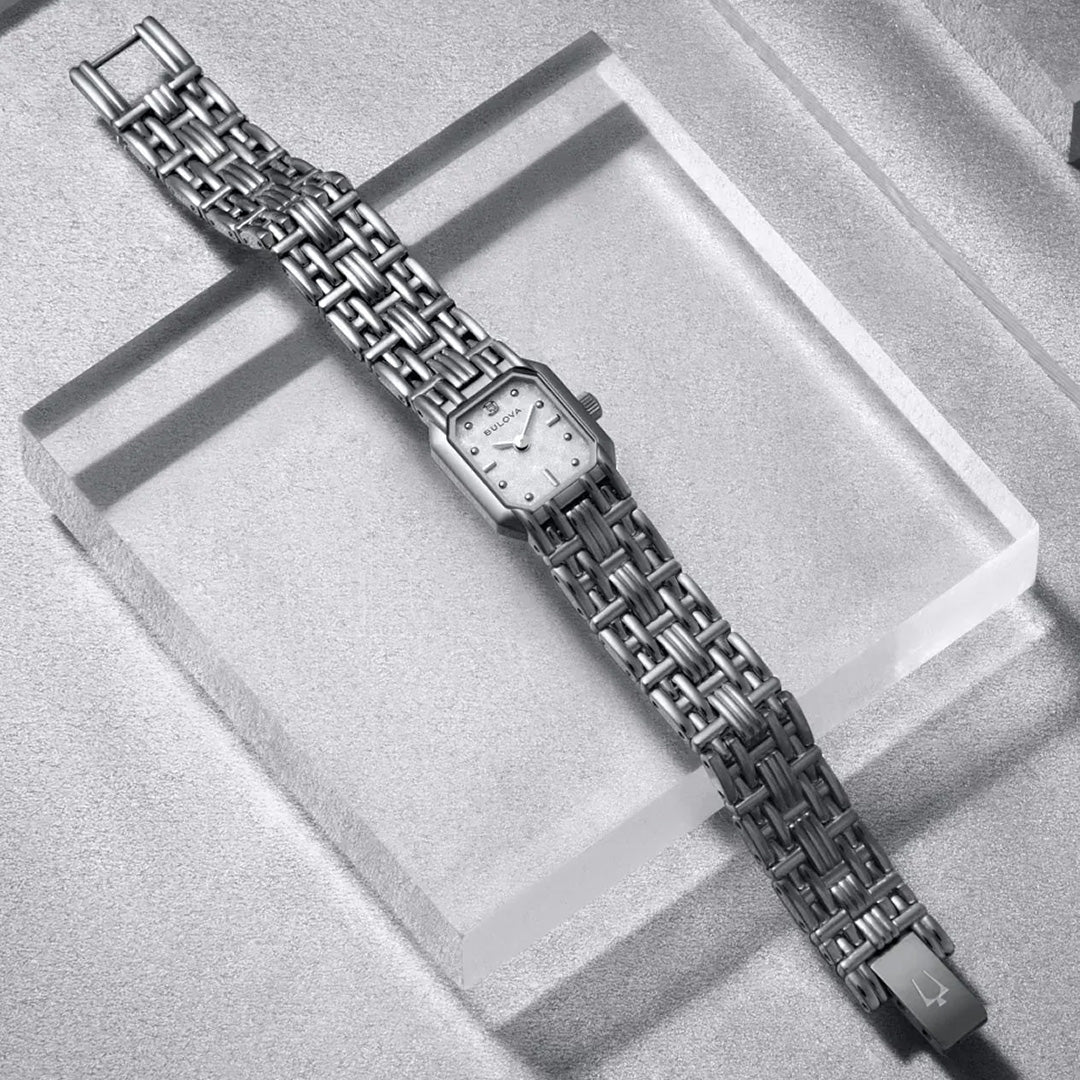 A Bulova Goddess of Time Sophia Quartz 16mm women’s watch, featuring a silver square face and metal link band, is displayed on a textured, light-colored surface with raised rectangular platforms.