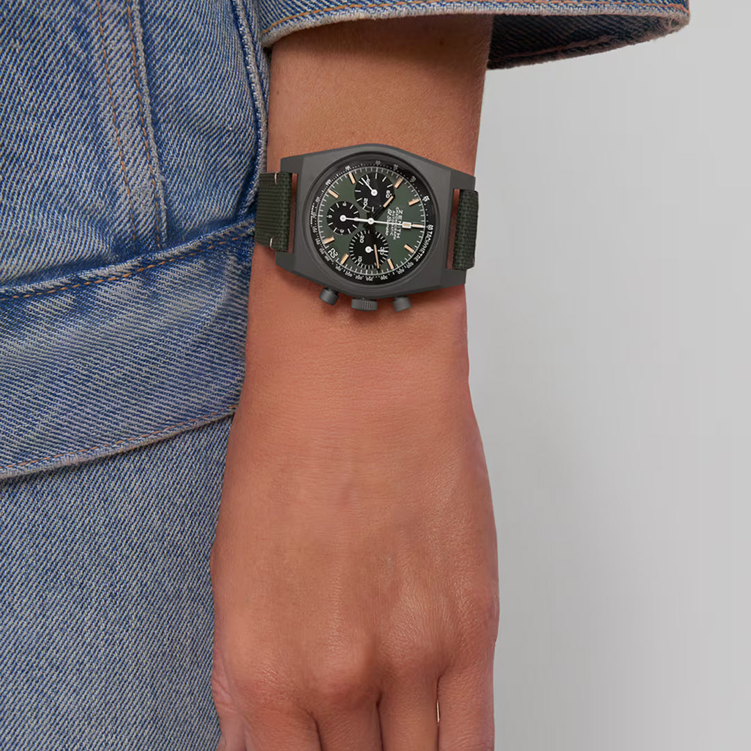 A close-up of someone wearing the ZENITH Chronomaster Revival El Primero 400 37mm watch on their left wrist, featuring a multi-dial face and dark strap in a titanium tonneau case. They are dressed in blue denim, with a visible sleeve seam.