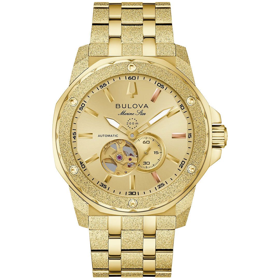 The Bulova Marine Star Marc Anthony Automatic 44mm men’s watch features a gold-tone case, metallic band, textured bezel, open-heart window, sub-dial at 5 o’clock, and "Marine Star" branding on the gold dial.